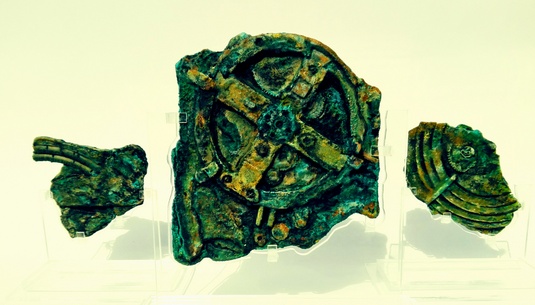 Fragments of the Antikythera Mechanism displayed in a museum, showcasing its corroded bronze gears and intricate design.