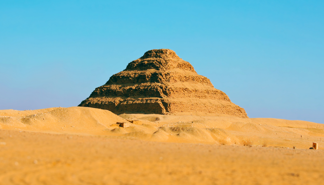 Step Pyramid of Djoser in Saqqara, Egypt, standing in the desert under a clear blue sky.