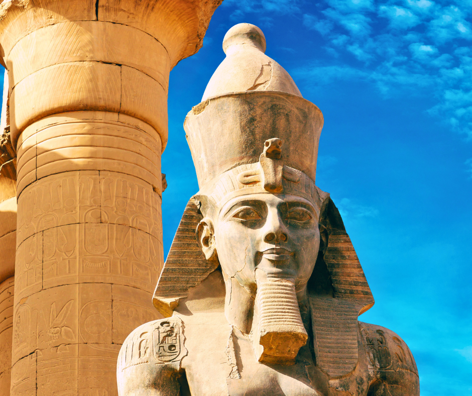 Colossal statue of Pharaoh Ramses II at the entrance of the Temple of Luxor in Egypt, framed by ancient columns under a clear blue sky.