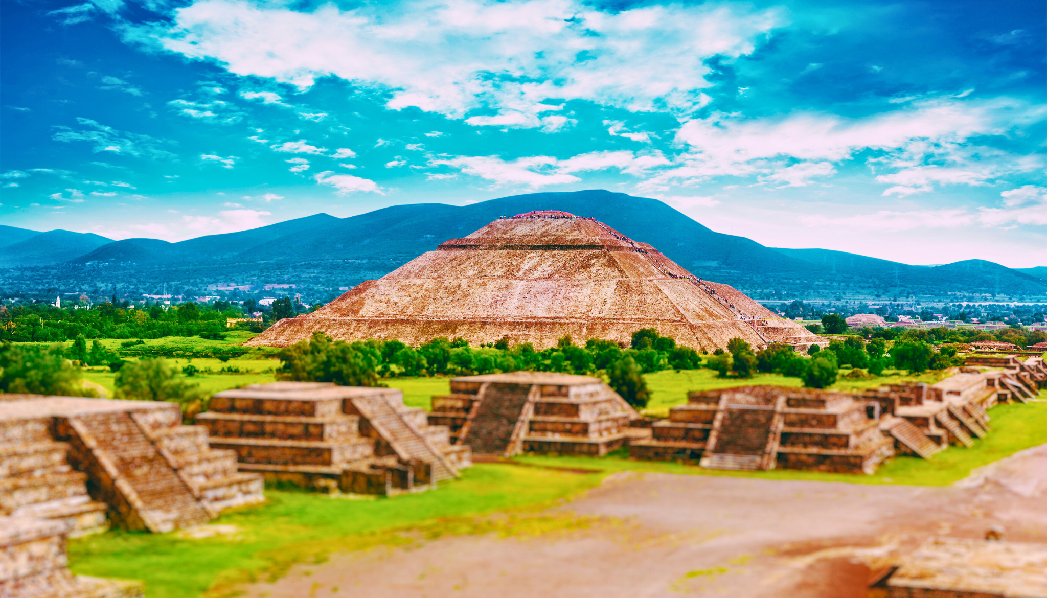 View of the Pyramid of the Sun at Teotihuacan in Mexico, surrounded by ancient stone structures and green landscape under a vibrant sky.
